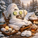 A white vintage-style sewing machine wrapped in white towels, with cucumber slices in its 'eyes', set on a wooden table in a snowy outdoor spa-like scene with candles, slippers, a teapot, and bath accessories.